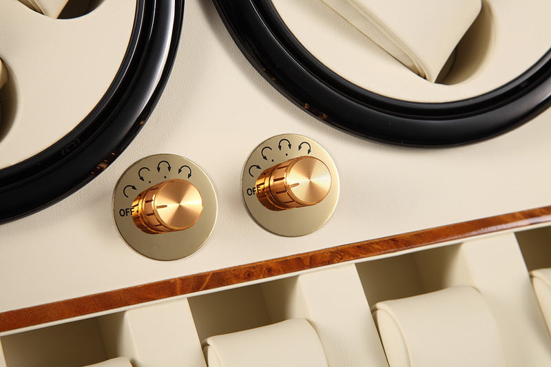 Watch winder close-up showing gold-tone knob controls and beige PU leather-wrapped interior
